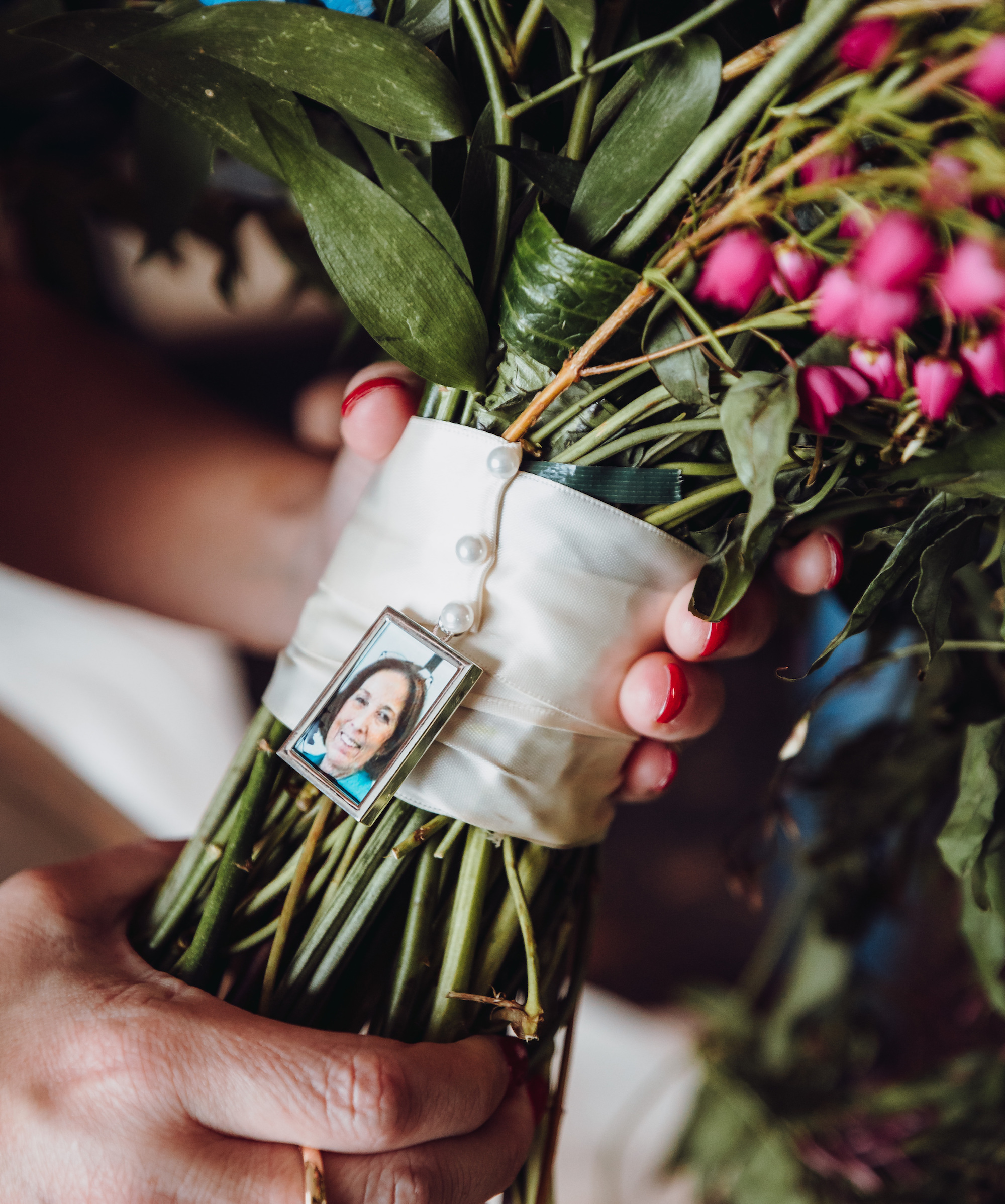 A bride holds her bridal bouquet which has a charm with a photo of her mother tied to the base of it.