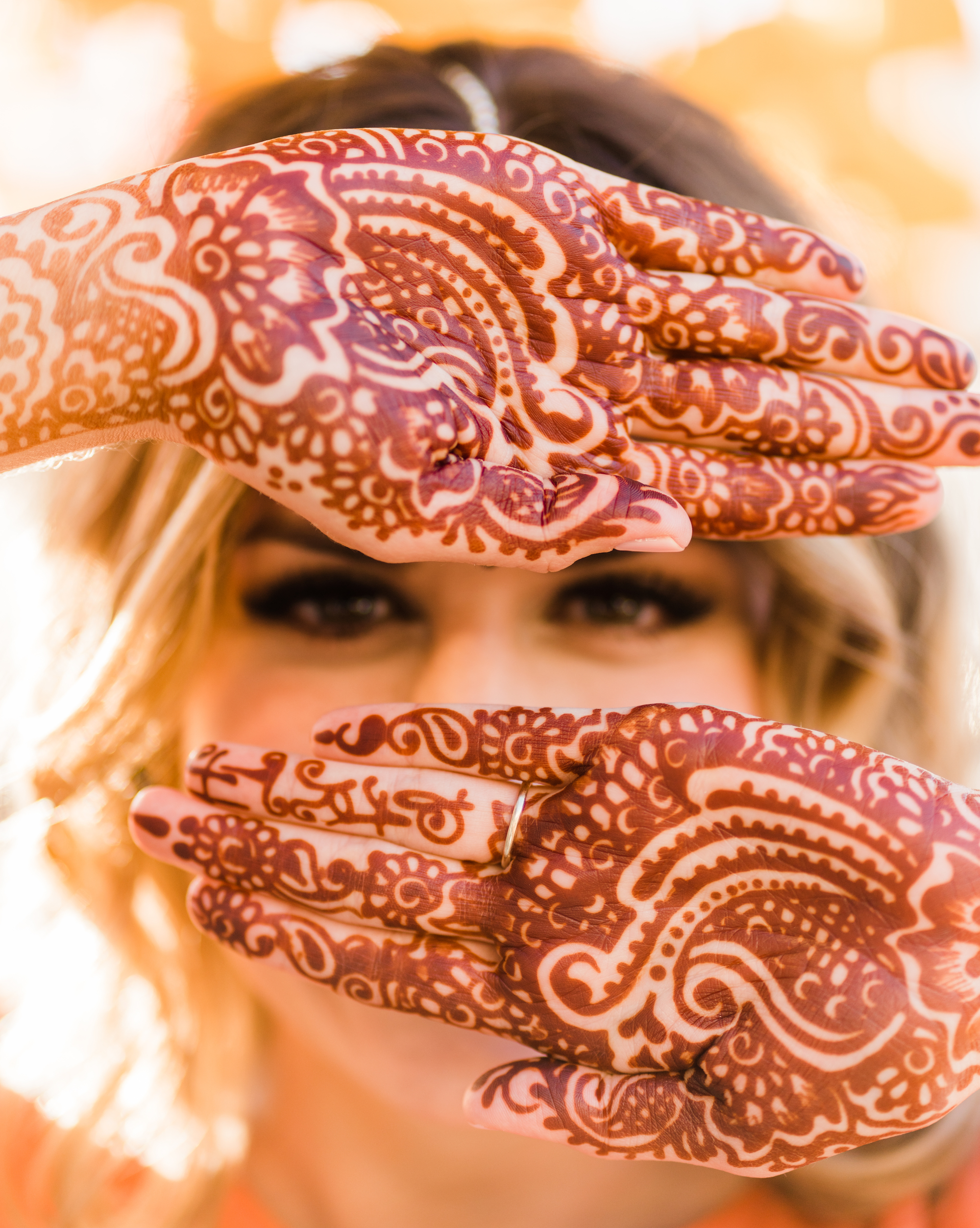 Bride poses with hands in front of her face with detailed henna tattoos. 