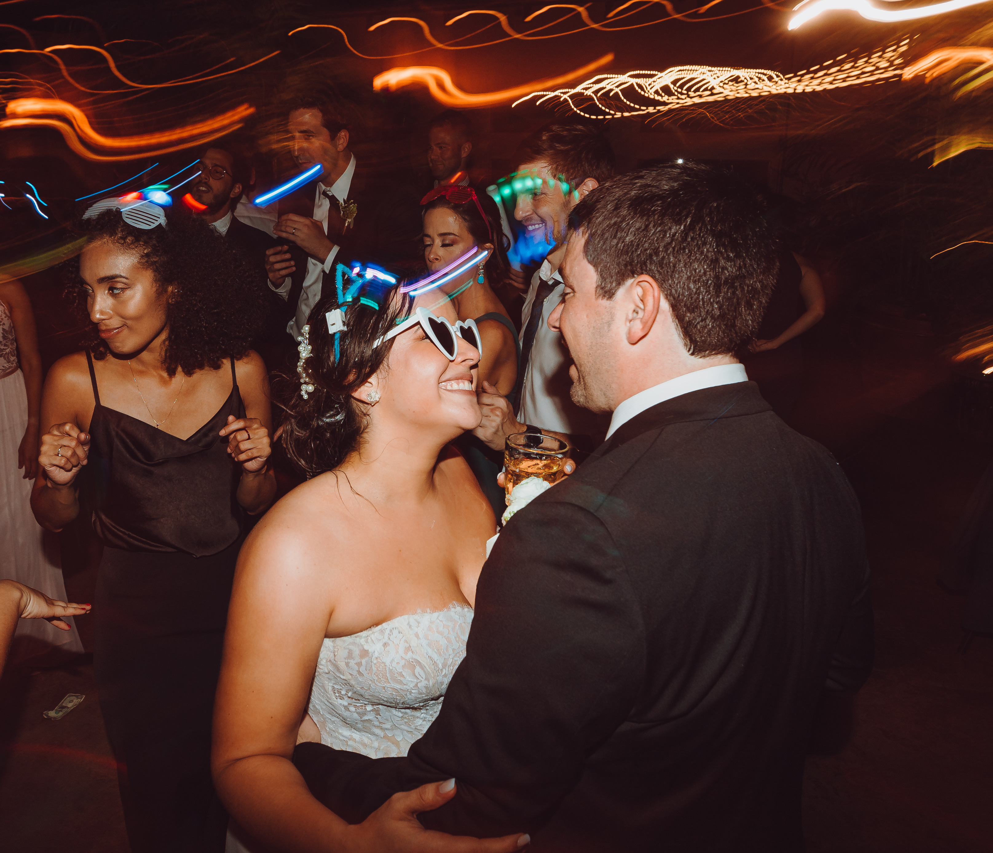 A bride and groom dance at their wedding reception in Houston. The bride wears heart shaped sunglasses and smiles at her groom.