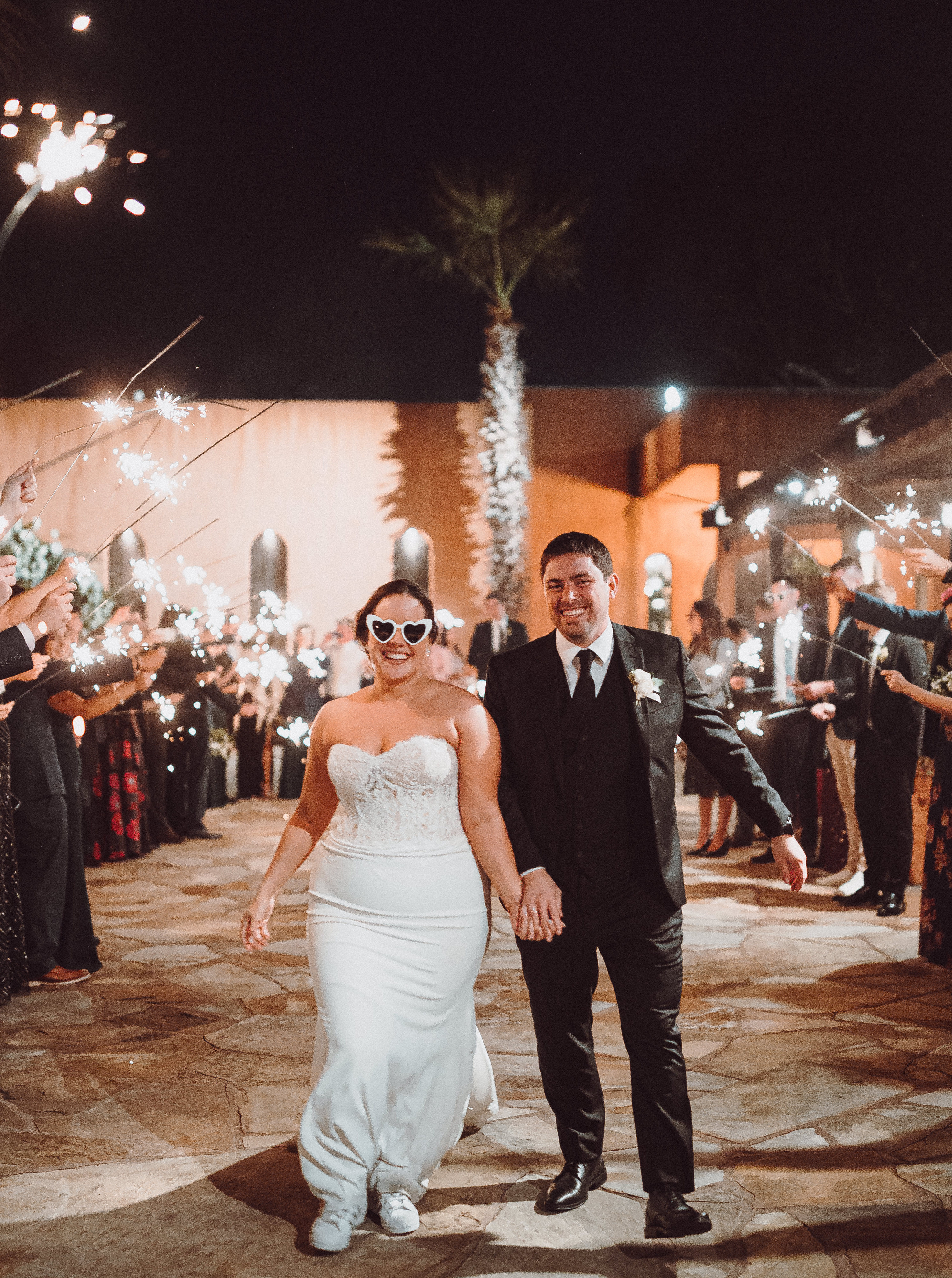 A bride and groom hold hands at their grand exit while their guests hold sparklers in the air.