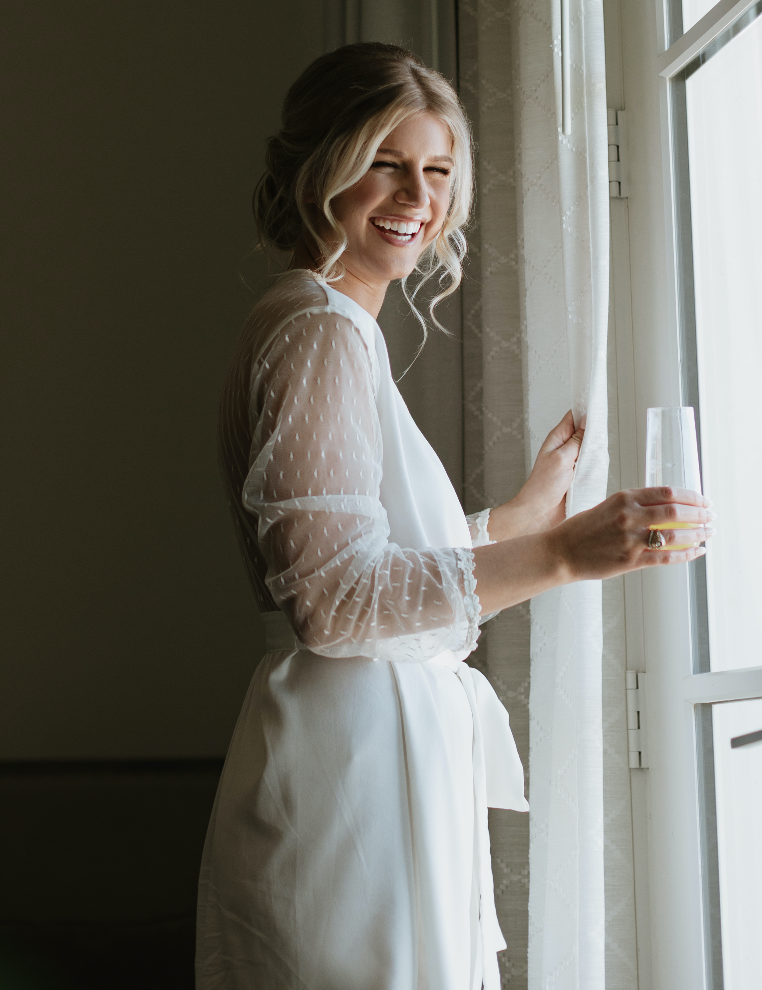 A bride smiles while in her robe getting ready for her peach-toned countryside wedding at Deep in The Heart Farms in Brenham, TX.