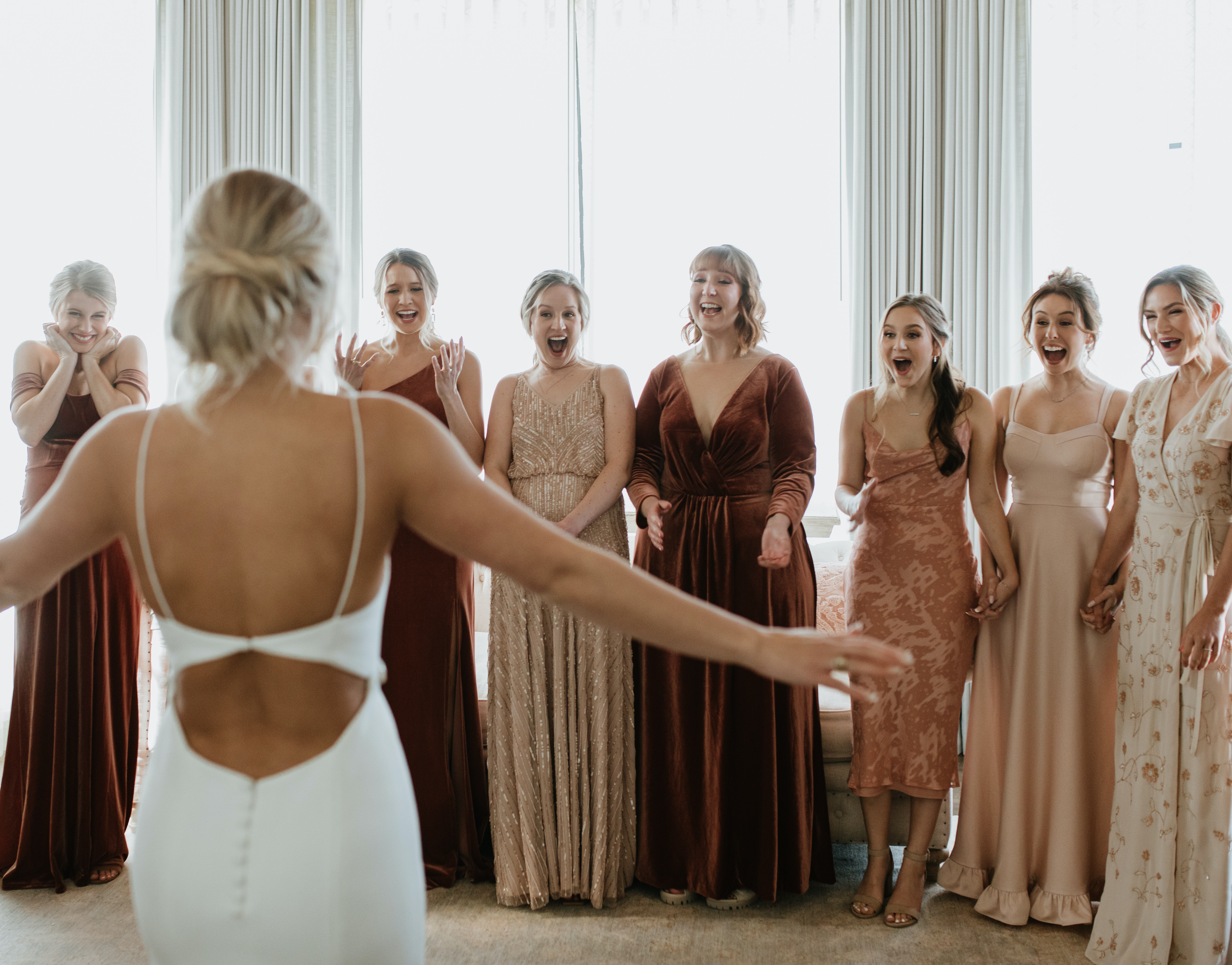 A bride reveals her full wedding day look to her bridesmaids who all smile at her. Peach-Toned Countryside wedding.