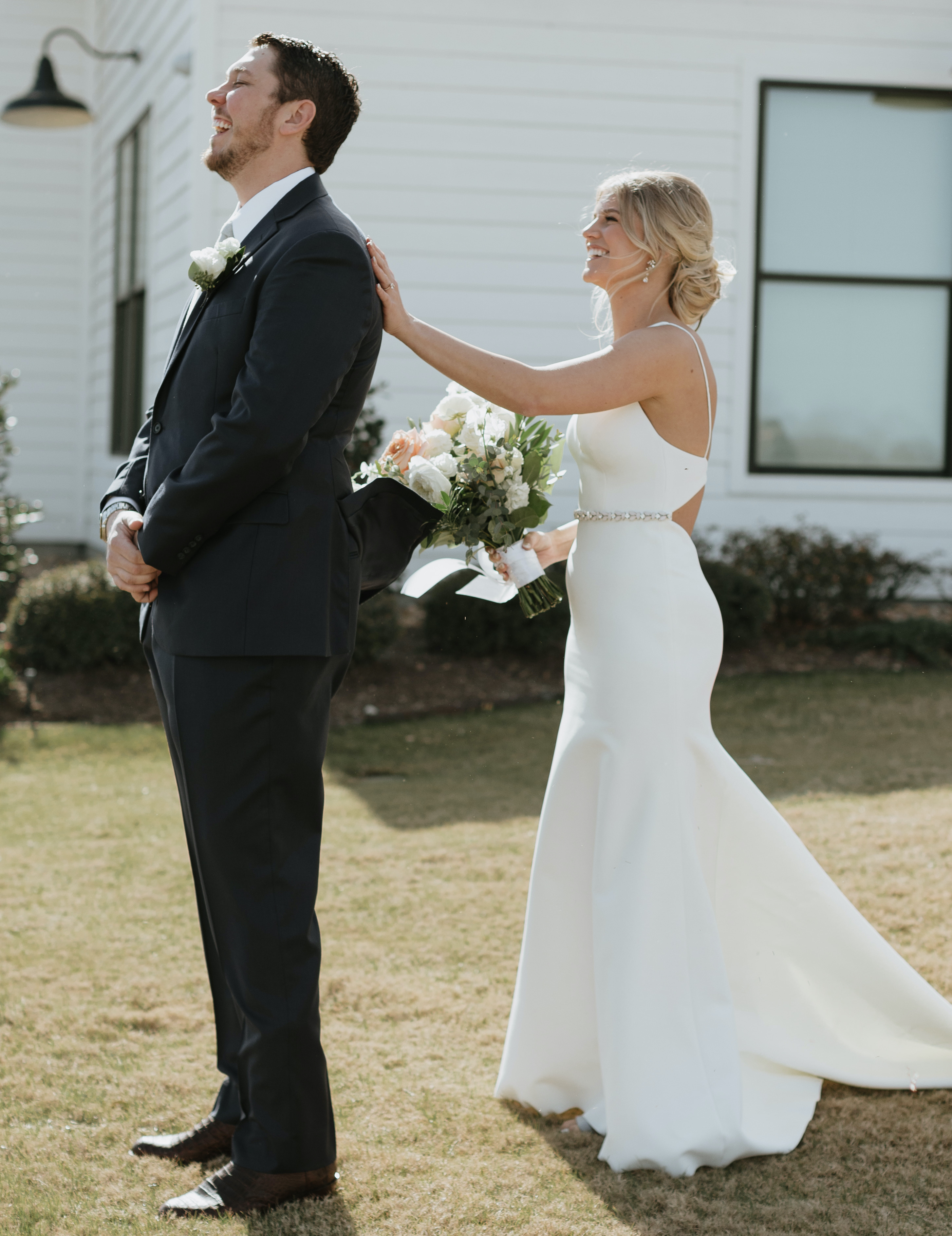 A bride taps her groom's shoulder while his back is facing her.