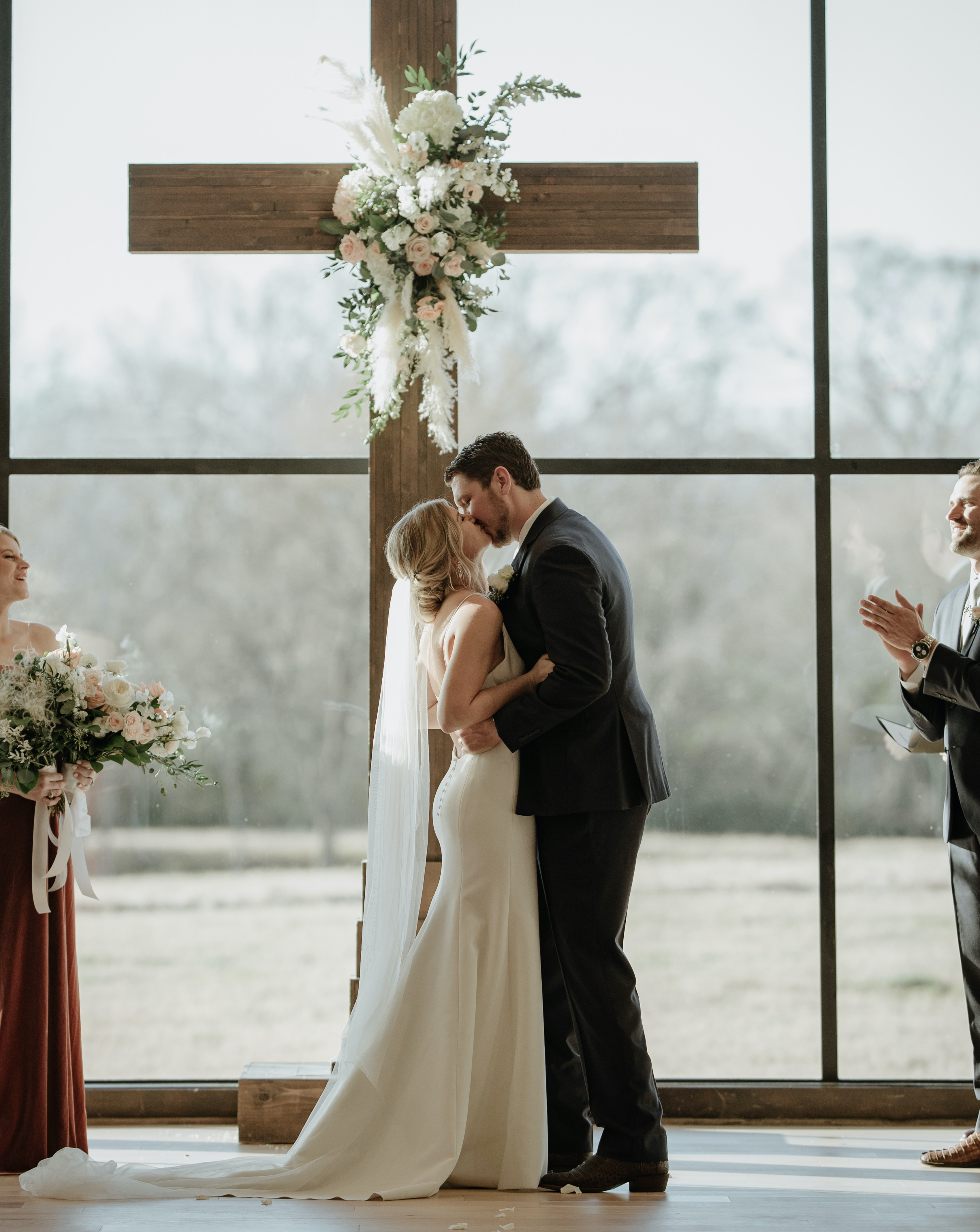 A bride and groom kiss at the altar during their peach-toned countryside wedding in Brenham, TX at Deep in The Heart Farms.