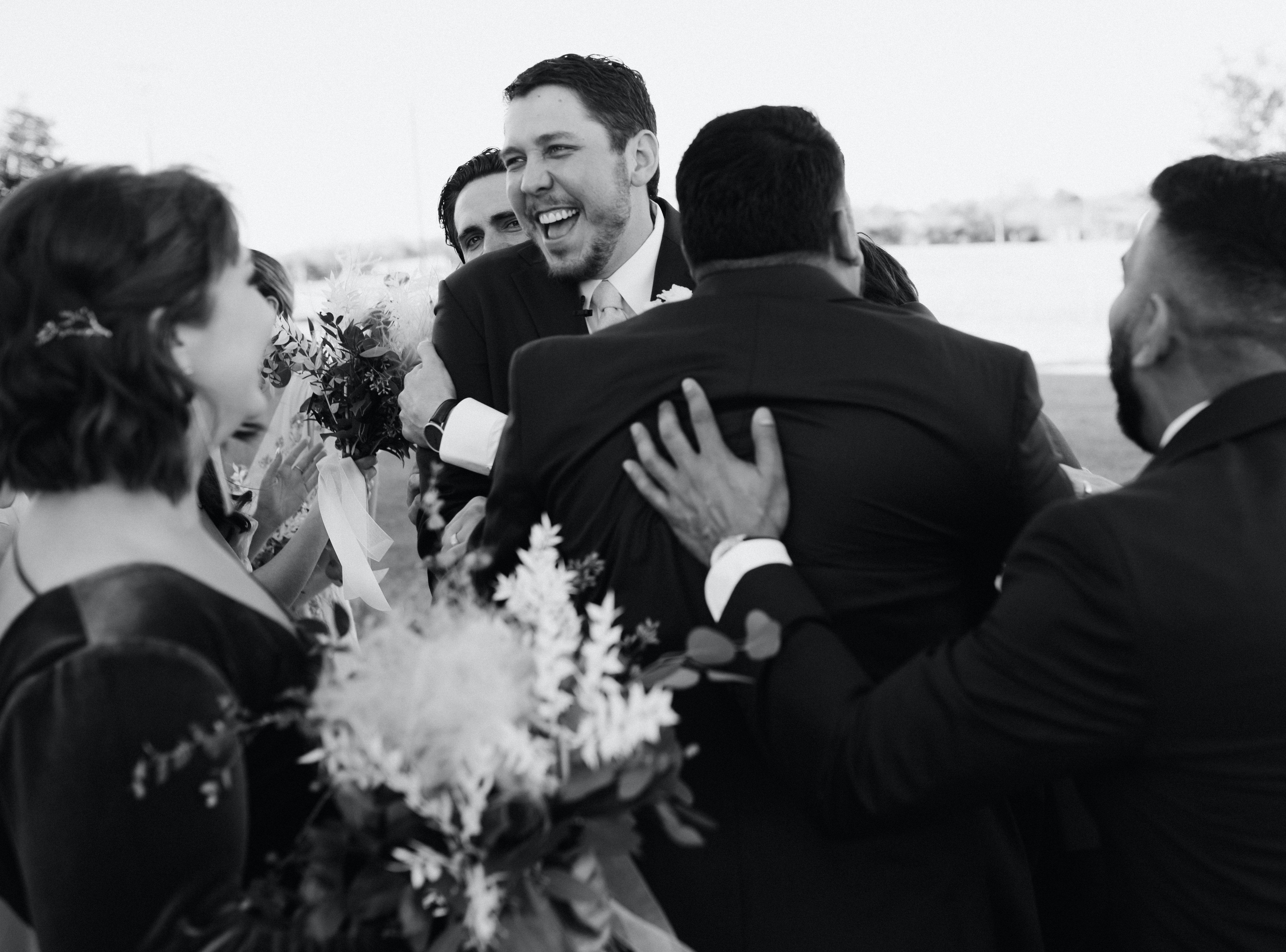 A black and white photo of a groom cheering with his groomsmen after he just got married in Brenham, TX.