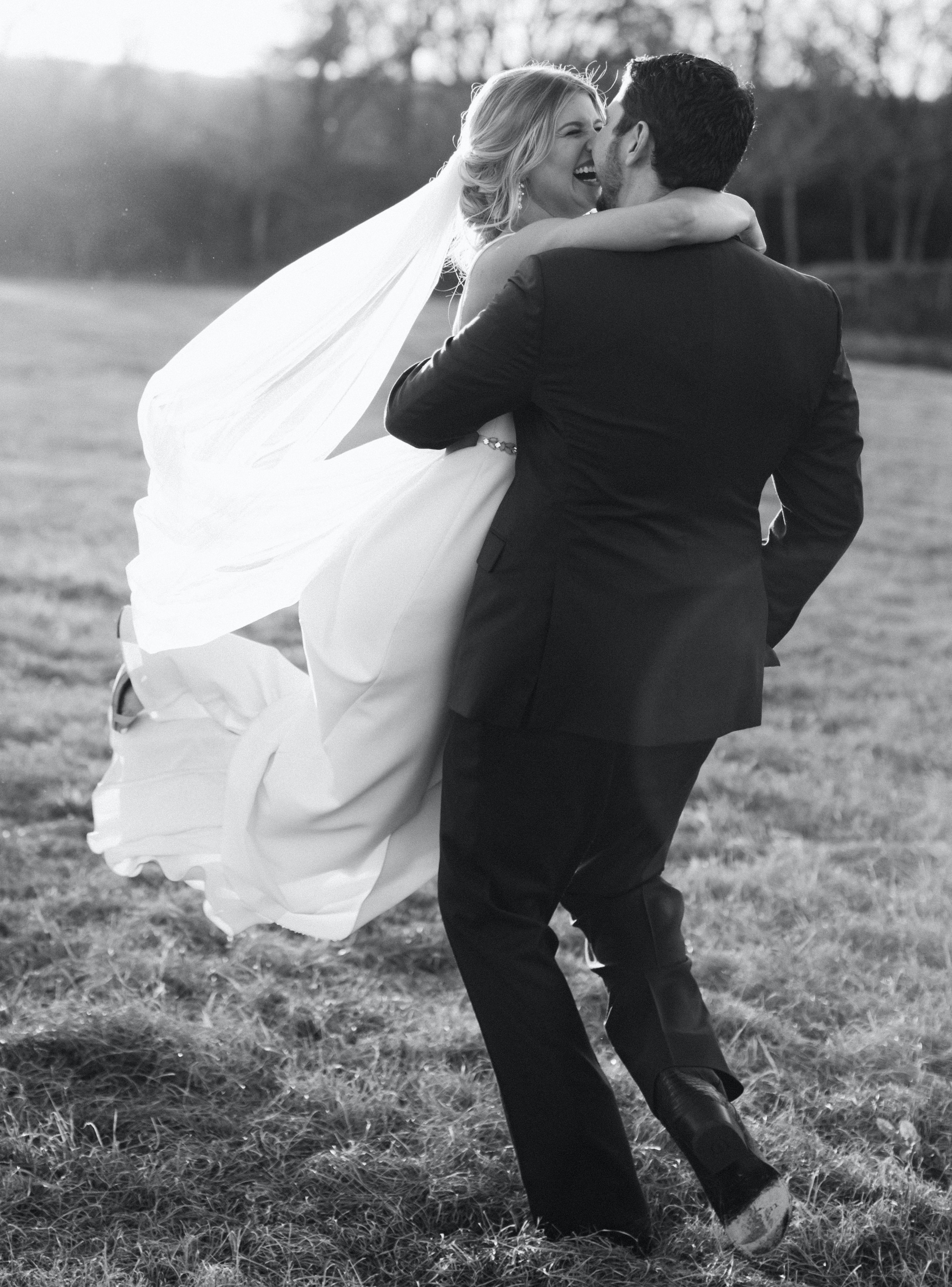 A black and white photo of a groom twirling his bride in a field in Brenham, TX during their peach-toned countryside wedding.