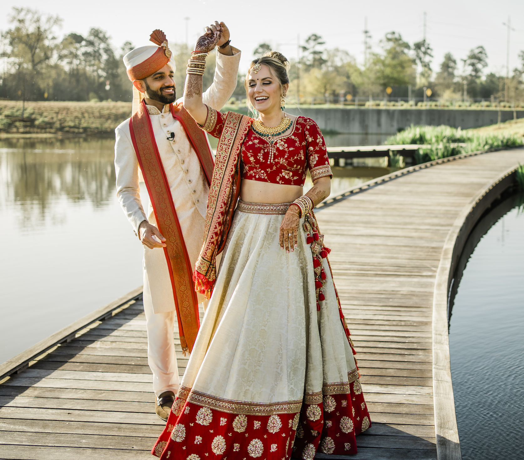 The bride and groom wearing traditional Indian wedding attire dance outside their wedding venue. 
