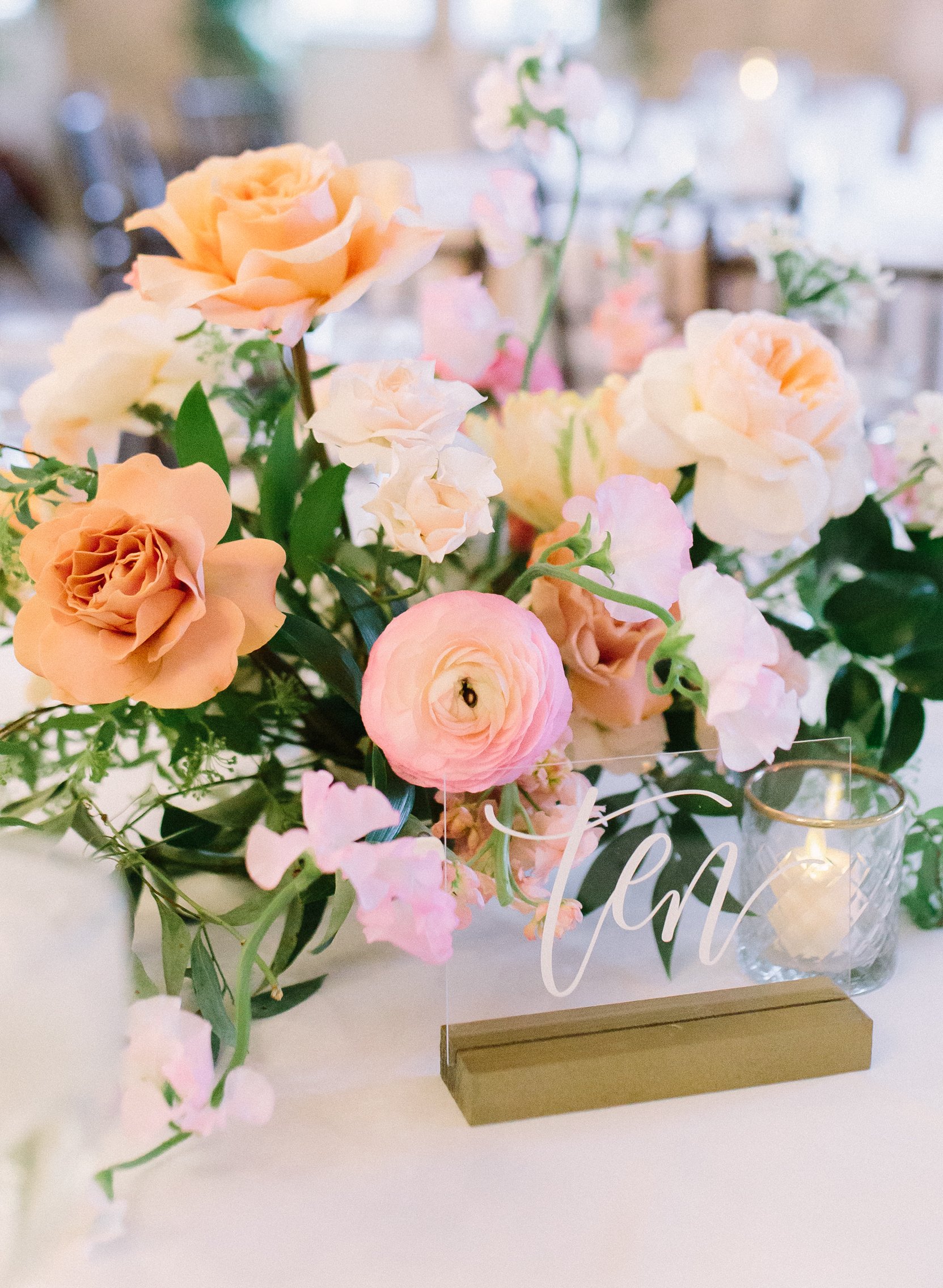 A centerpiece sits on a table for a wedding reception with peach and pink flowers.