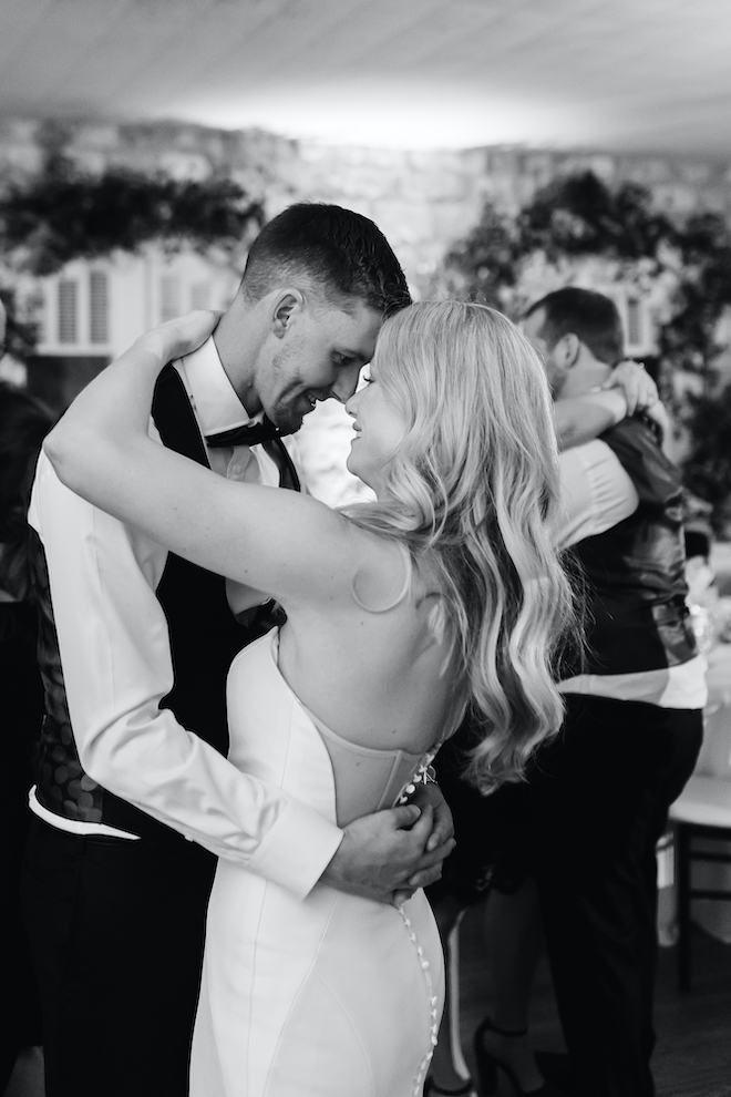 A black and white photo of the bride and groom looking into each others eyes as they dance at their wedding reception. 
