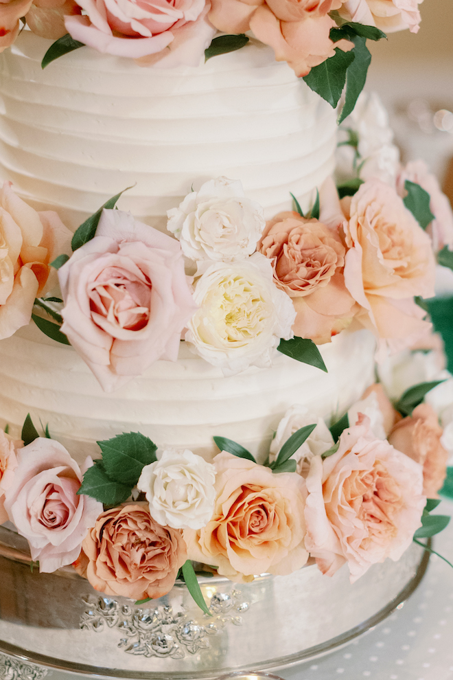 A 3-tier white wedding cake on a silver tray is decorated with pink, cream and orange flowers. 