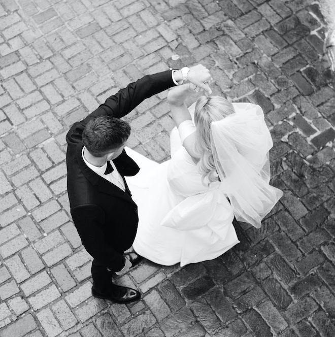 A black and white photo of the groom spinning around his bride outside of the church. 