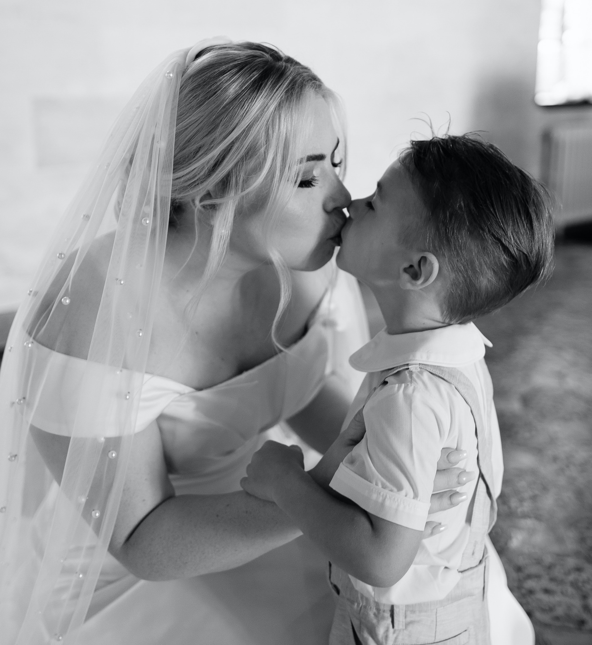 A bride with a pearl embellished veil kisses a young flower boy on her wedding day in Florida. 