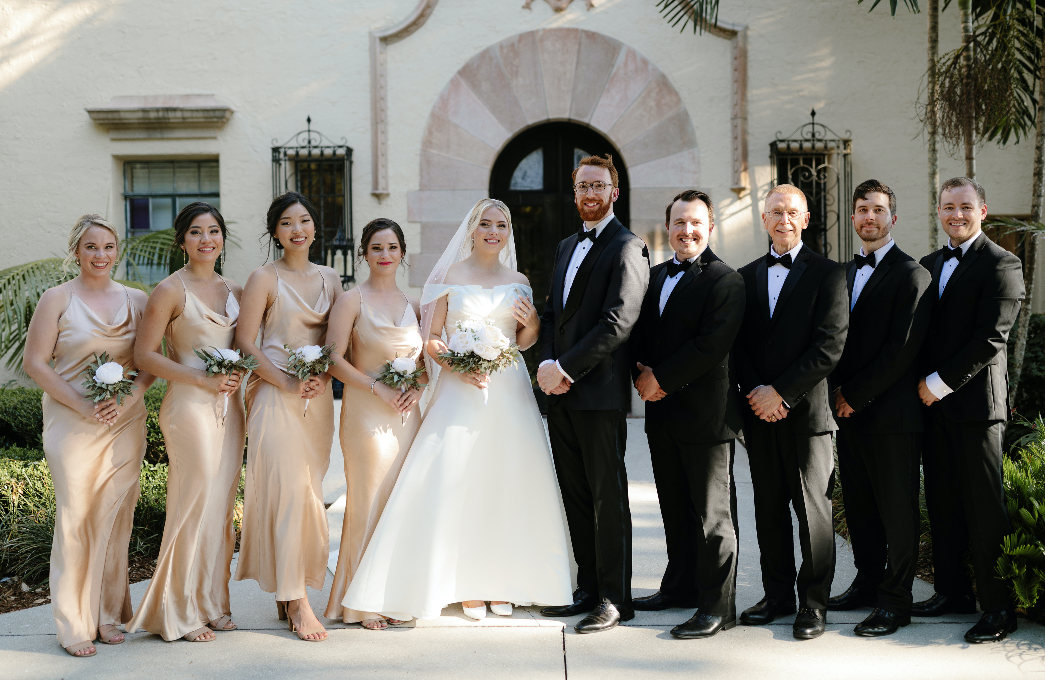 A bride and groom stand with their bridesmaids and groomsmen outside of their wedding venue in Sarasota, FL.