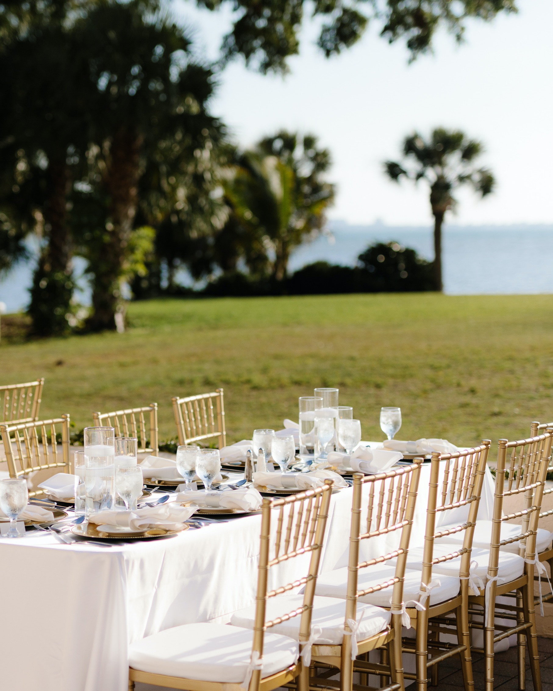 A family style table with gold chiavari chairs on the lawn of a waterfront estate in Sarasota Florida. 