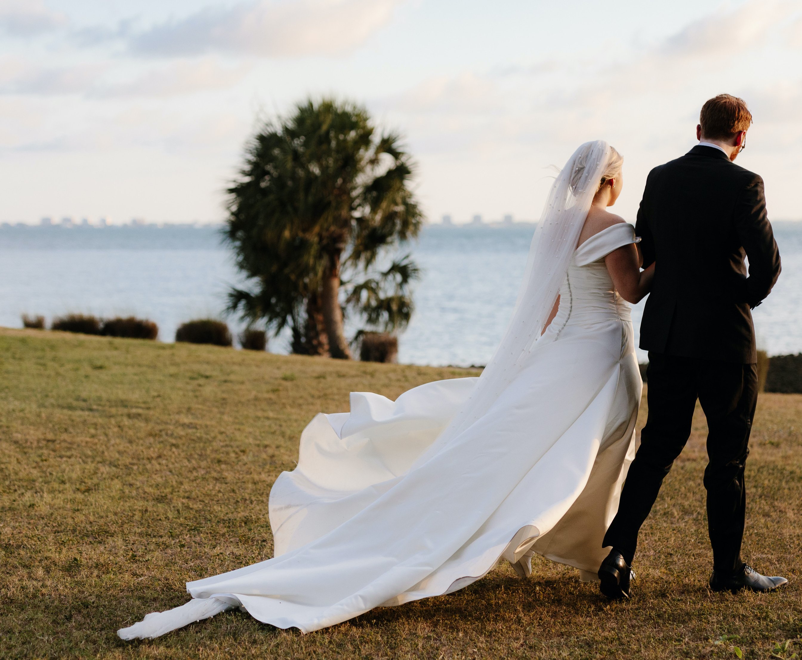 A bride and groom walk on a lawn overlooking Sarasota Bay in Florida during their intimate alfresco summer wedding.
