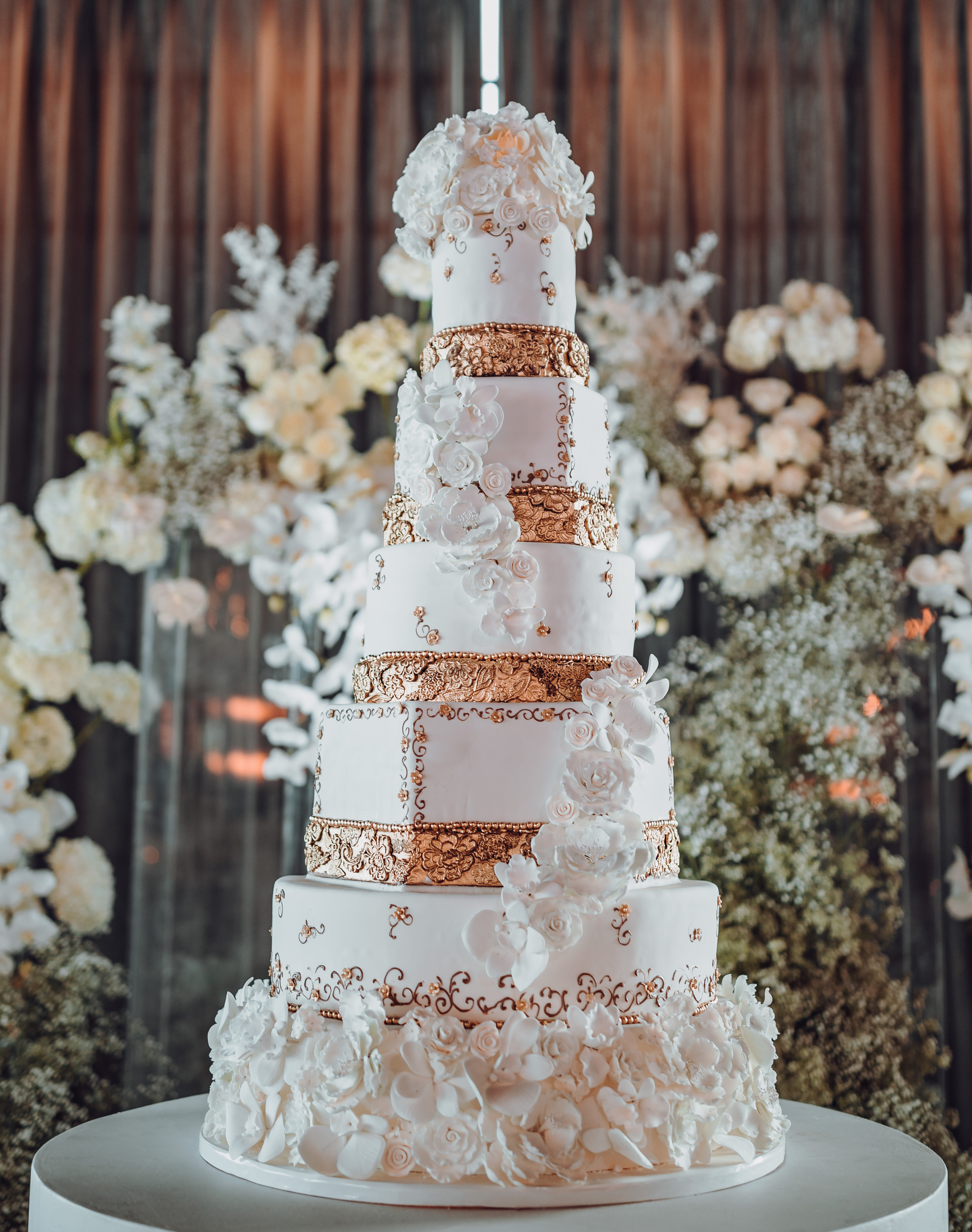 A 6-tier cake with white frosting, gold leaf accents and fondant roses at a real wedding at Houston venue, The Astorian. 