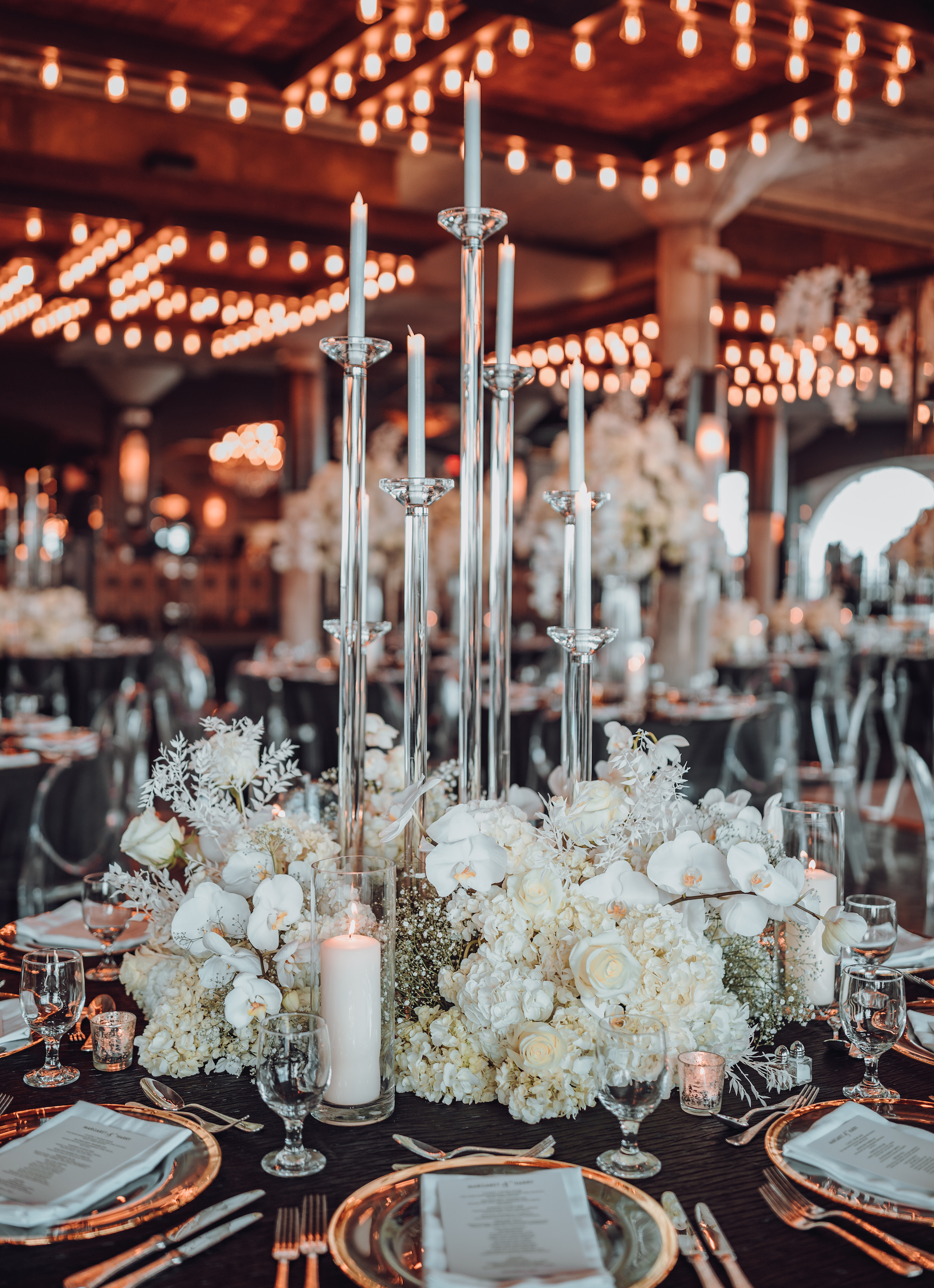 A centerpiece is set up with tall candles and white flowers for a white, gold and black wedding at The Astorian in Houston, TX.