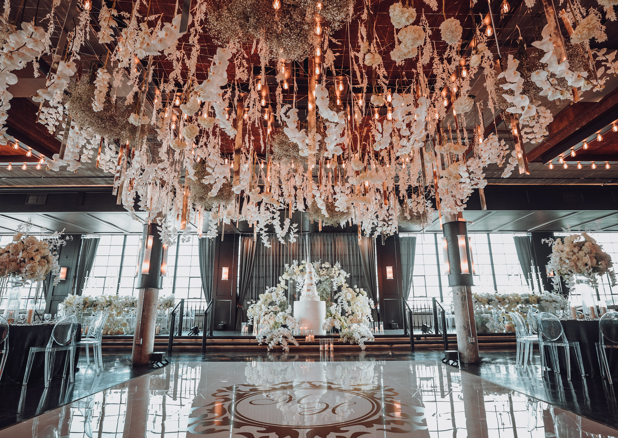 A reception room is decorated with white orchids hanging from the ceiling and all around the tables for a white, gold and black wedding in Houston, TX.