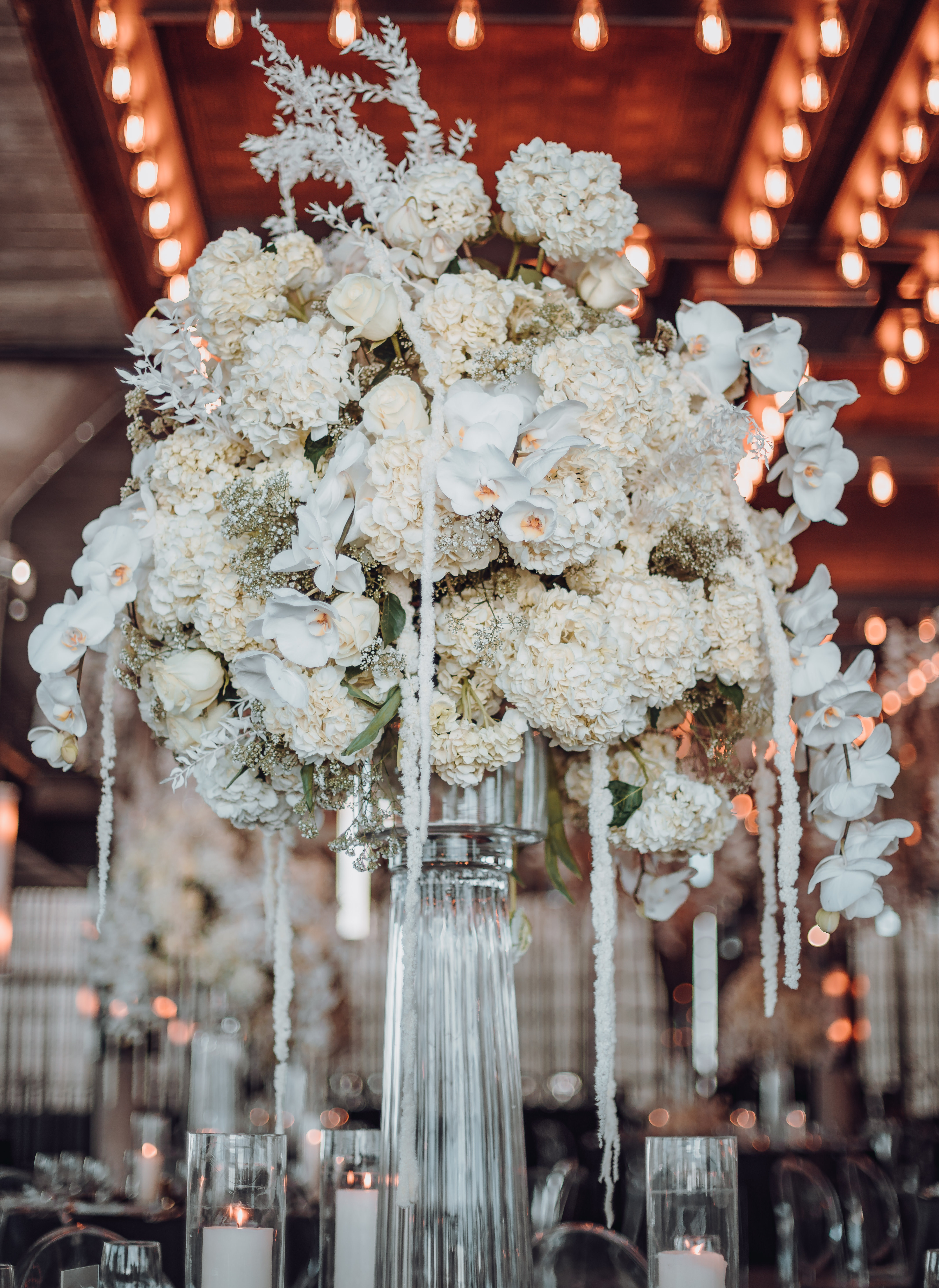 A tall centerpiece at a wedding reception with white flowers in it.