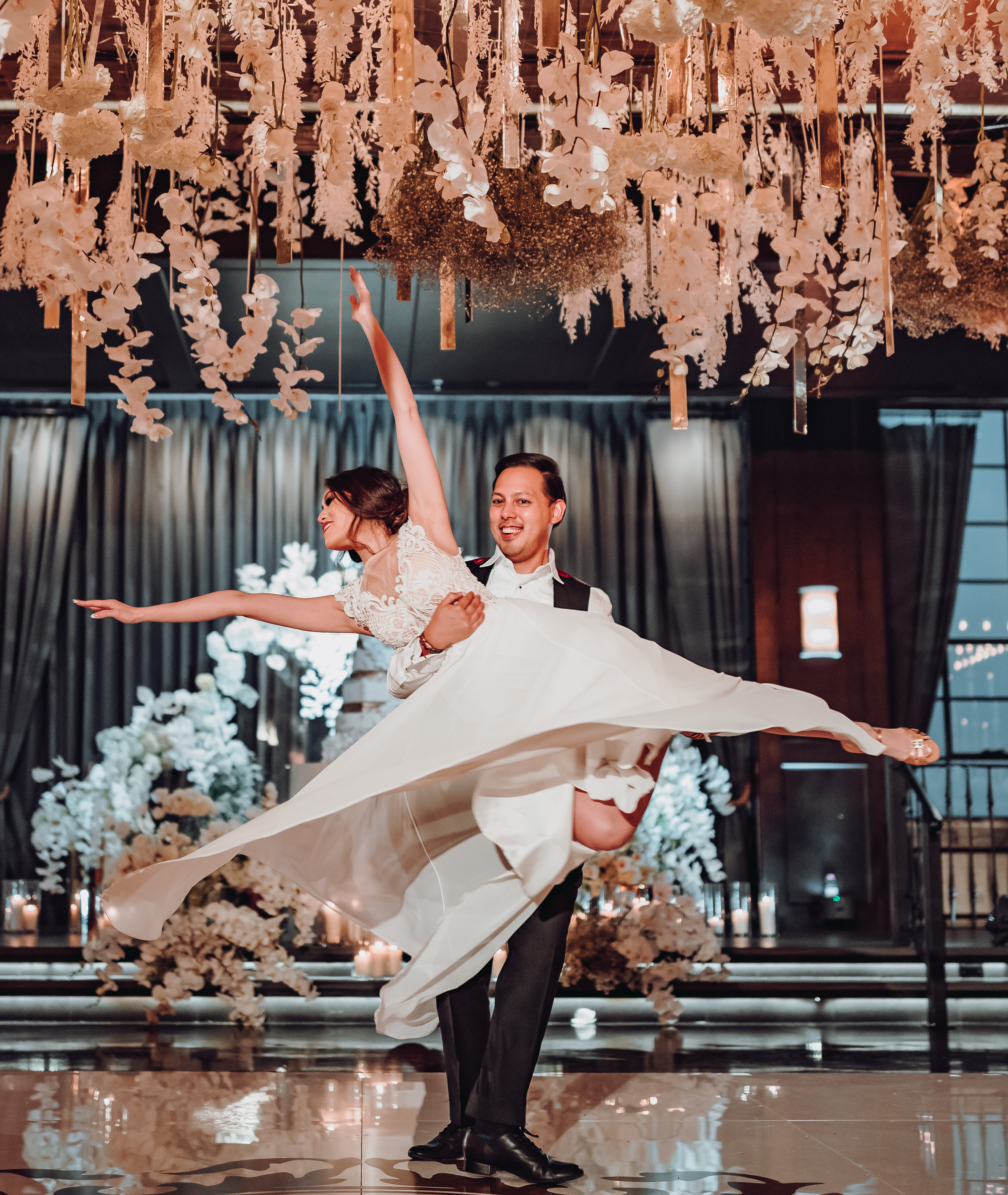 A groom picks up his bride as her dress spins in the air and her hands are up as they are dancing at thier wedding at The Astorian in Houston, TX.