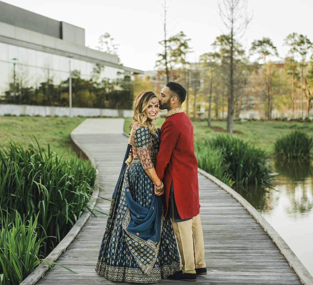 Groom in wedding kurta kisses a bride in a bridal saree on the evening of their sangeet at Marriott Cityplace at Springwoods Village. 