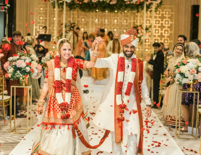 Bride and groom walk down a rose petal strewn aisle hand in hand after their hindu ceremony at houston wedding venue, Marriott Cityplace at Springwoods Village. 