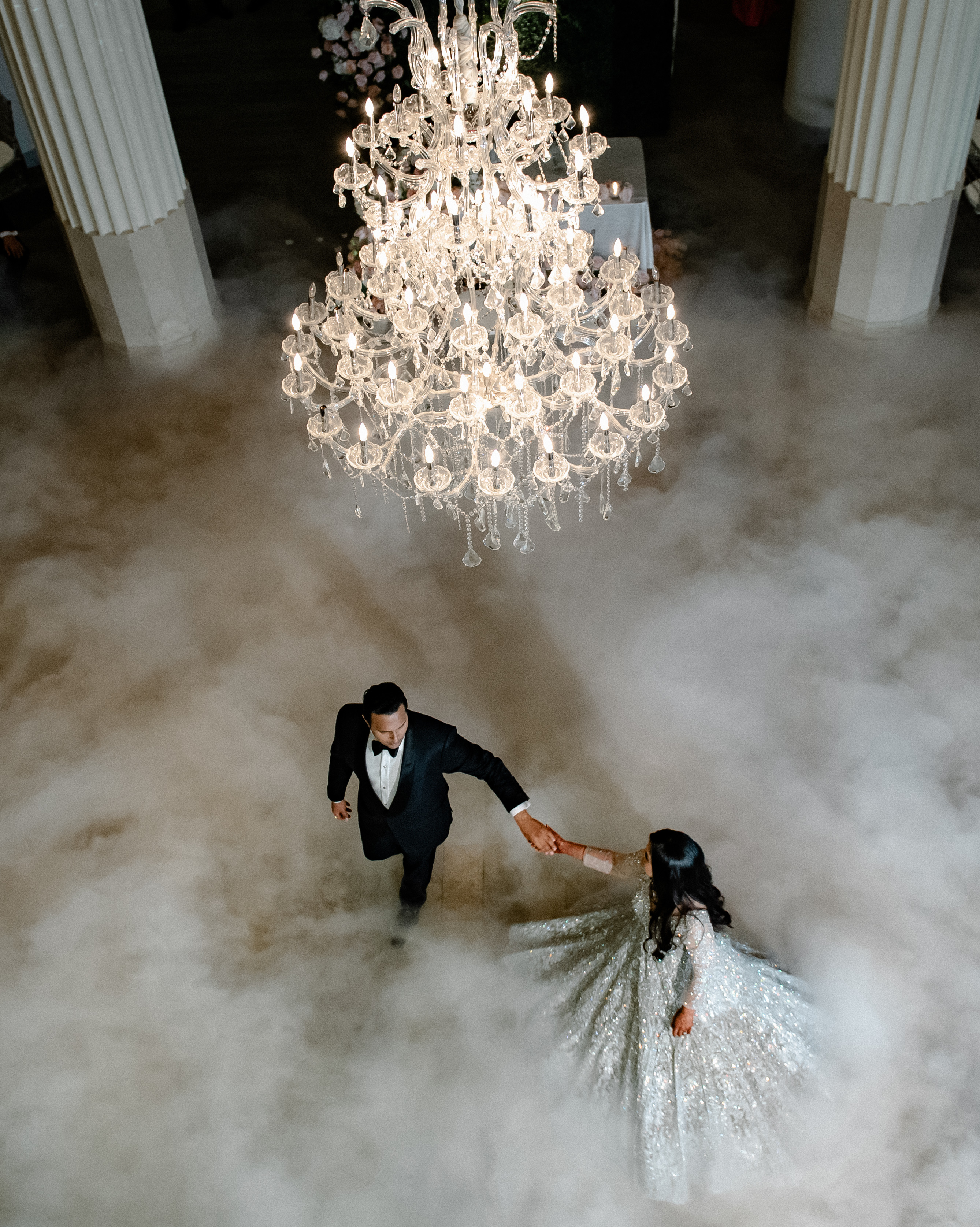 The bride and groom dance under a crystal chandelier with fog filling the dancefloor. 