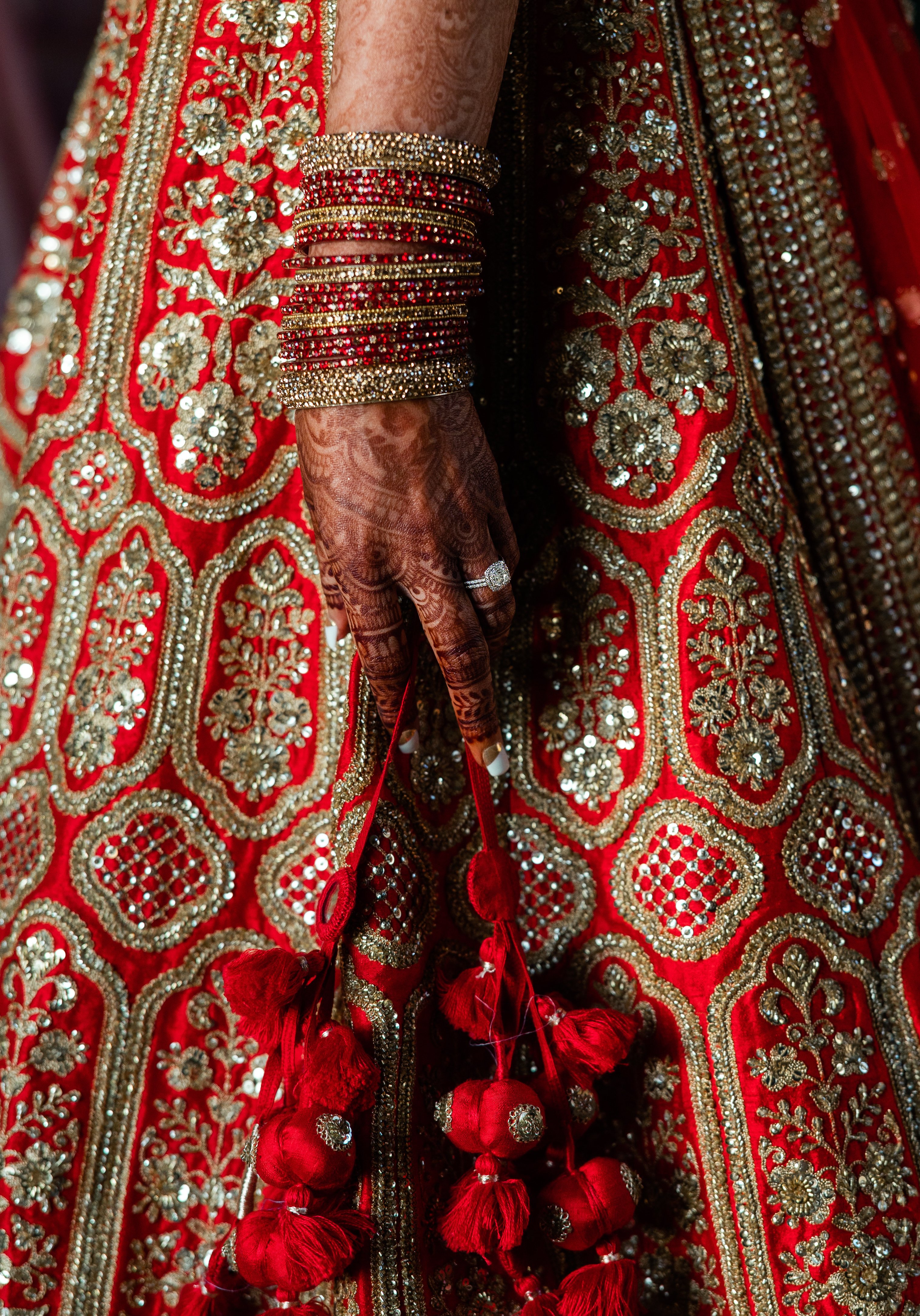 The bride's hand is detailed with henna and traditional red and gold Hindu bracelets. 