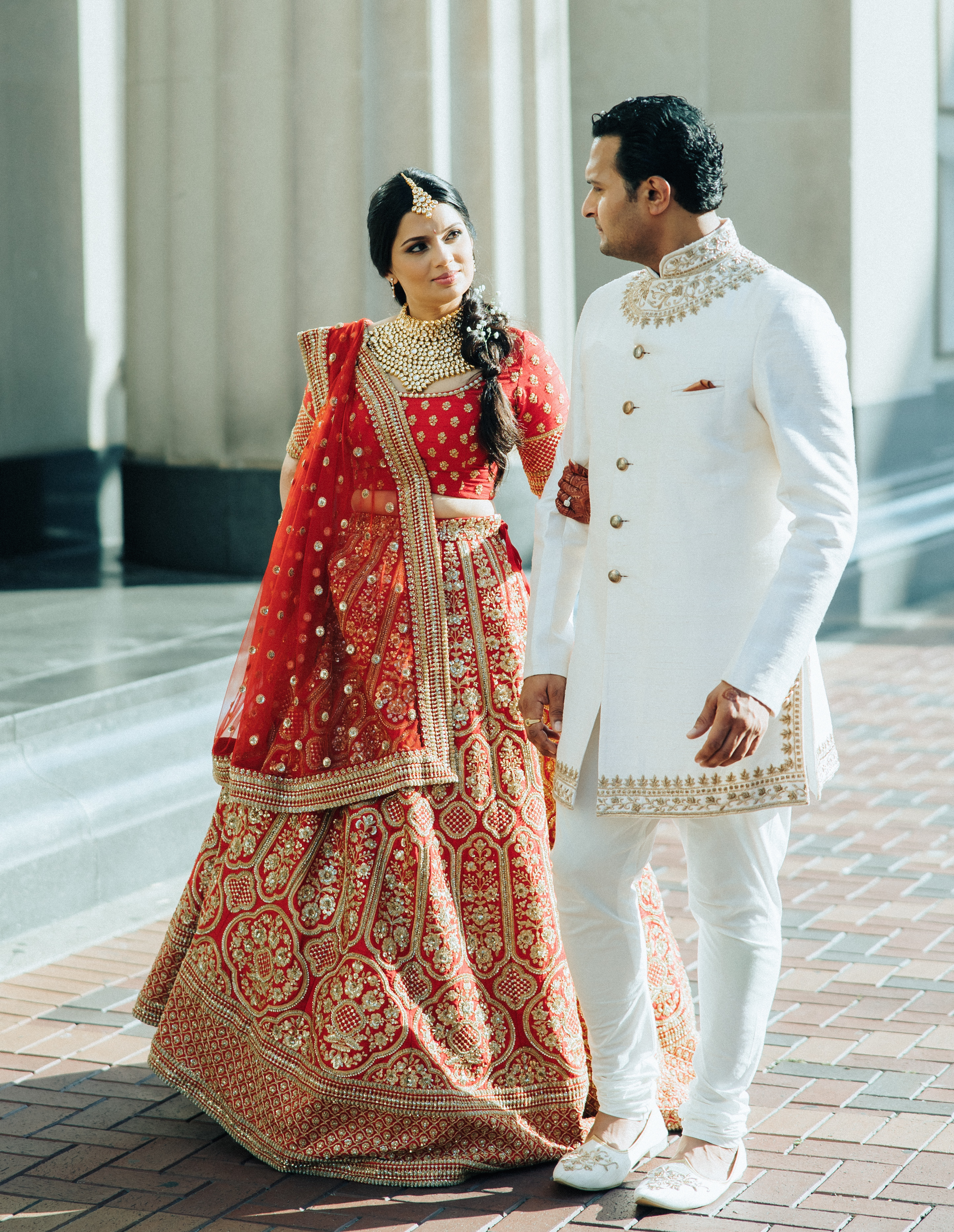 The bride and groom hold hands while dressed in traditional Hindu attire outside their wedding venue. 