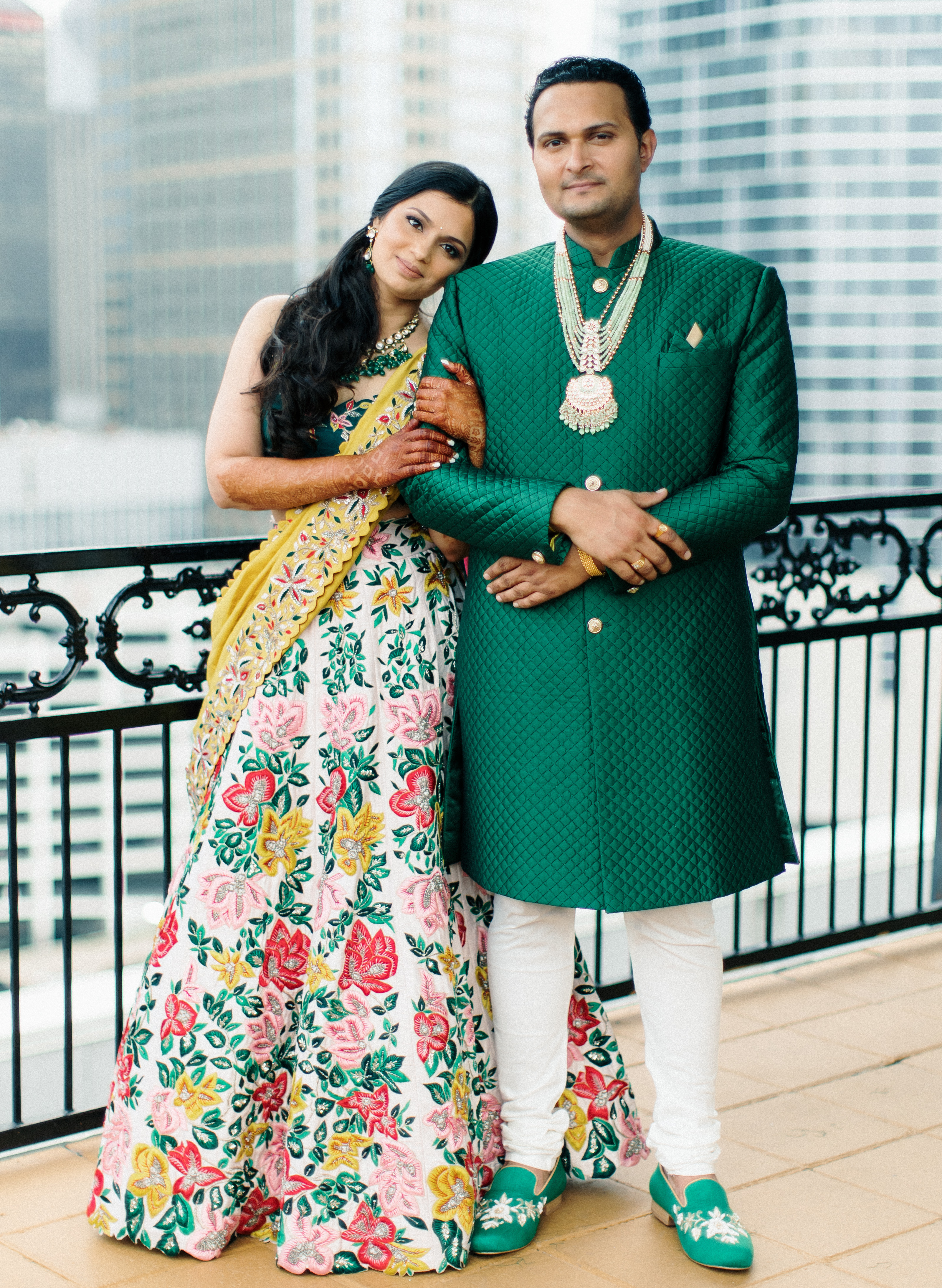 The bride and groom pose in traditional Hindu attire on the balcony of their wedding venue.