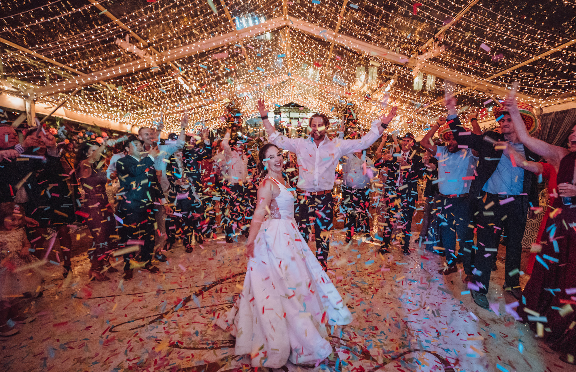 Colorful confetti is in the air while wedding guests cheer for the bride and groom at a wedding in Houston.