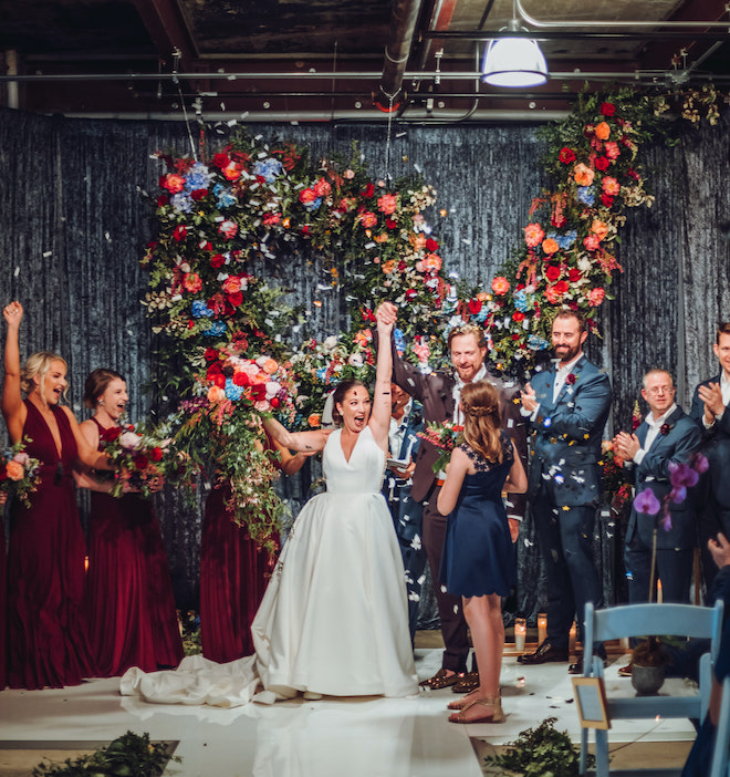 A bride and groom celebrate at the alter with their wedding party with confetti. 