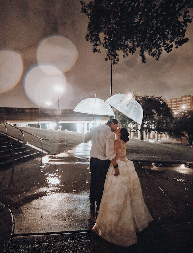 A bride and groom each hold umbrellas as they kiss in the rain in Houston, Texas. 