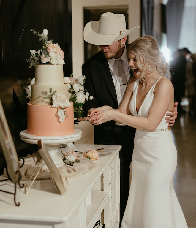 The bride and groom cut their peach, 3-tier wedding cake at their wedding venue, Deep In The Heart Farms. 