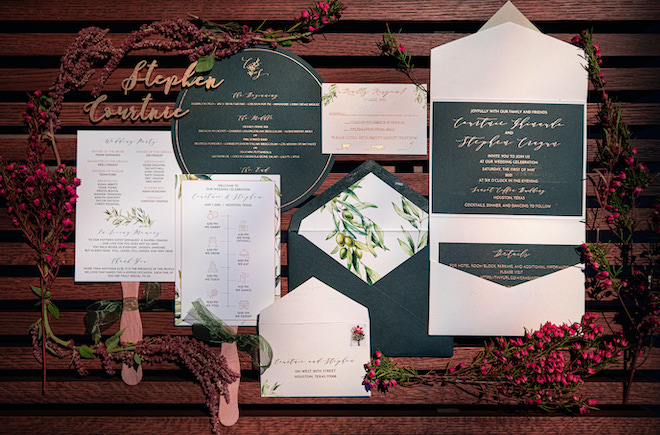 Blue and gold stationery and invitations displayed on would surface with red flowers and greenery. 