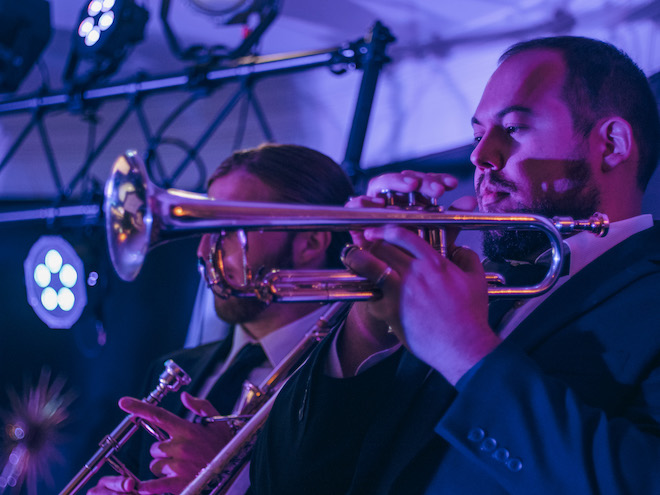 Two men from the live music and entertainment band, The Moment, play the trumpet at a wedding reception. 