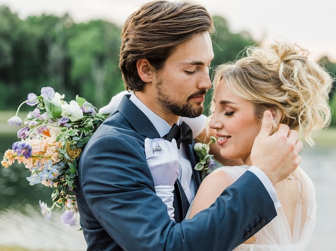 A bride looks over her shoulder while holding her bouquet around the grooms neck as he goes in to kiss her.