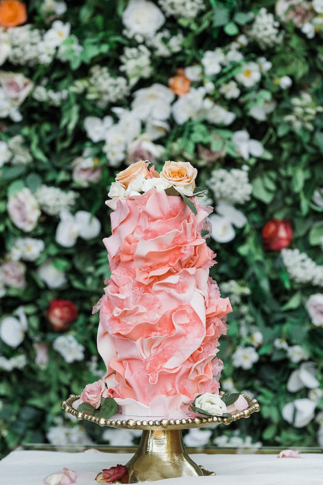 A pink and floral wedding cake sits on a gold cake stand. 