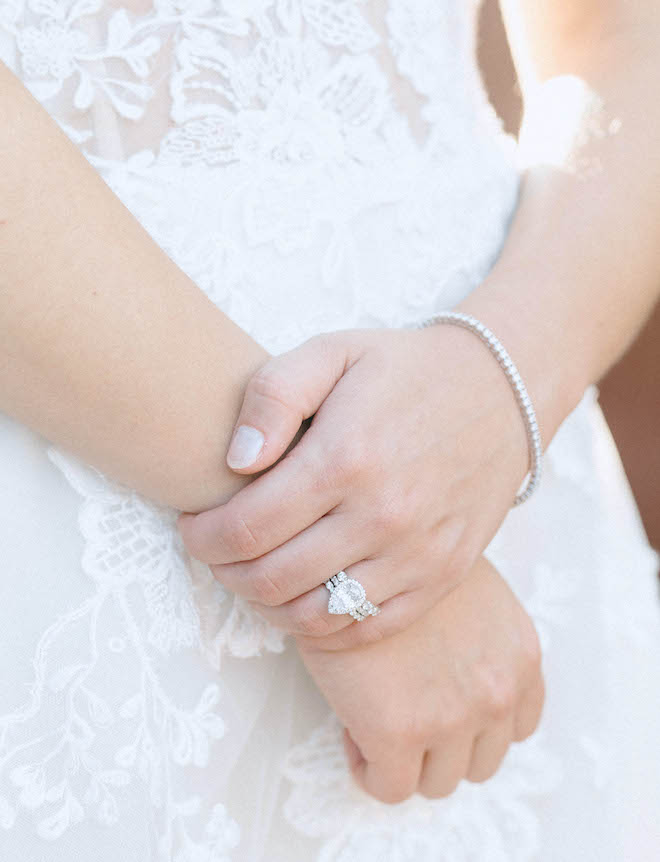 The bride holds her right wrist with her left hand while wearing an almond shape wedding ring and a diamond bracelet. 