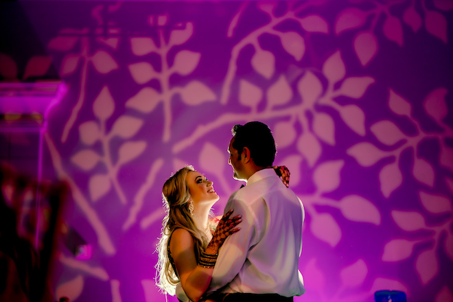 Bride and groom slow dance with a backdrop of purple lights.