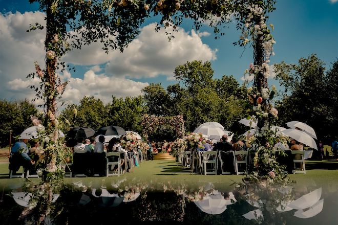 Guests holding umbrellas to block the sun while watching the wedding ceremony.