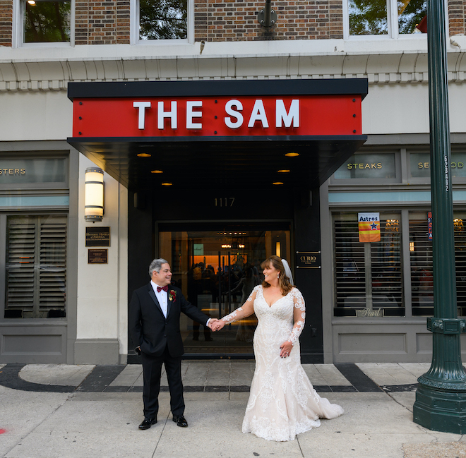 The couple holds hands in front of the Sam Houston Hotel