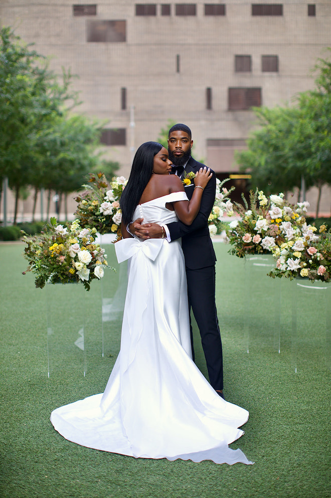 The couple posing in front of the ceremony setup, with the bow on the back of the brides modern gown showing.