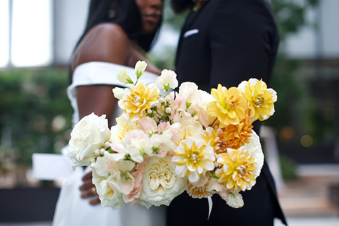 The couple in the background of a yellow, blush and white bouquet. 