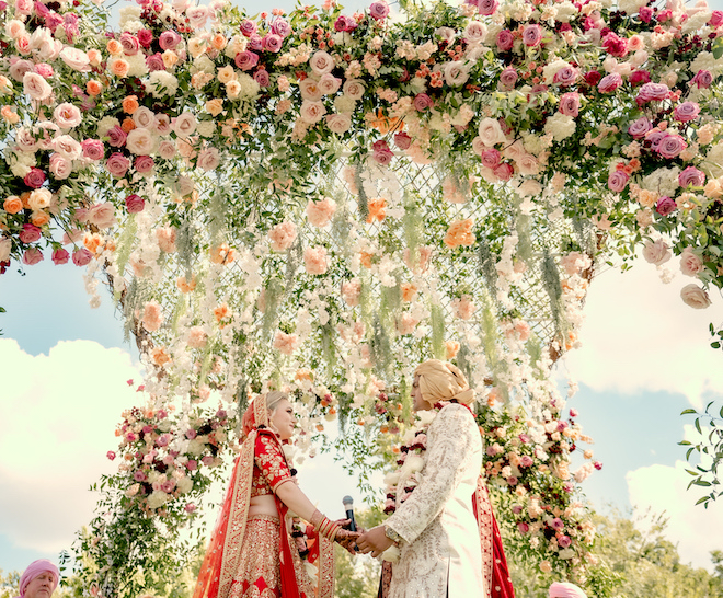 A smiling bride and groom holding hands underneath a floral Mandap on their wedding day at Hyatt Lost Pines in Bastrop, TX.