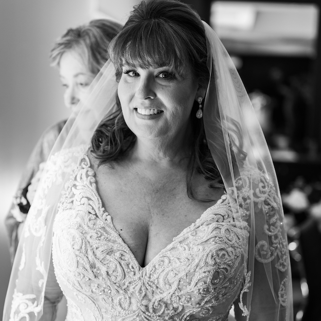 A black and white photo of the bride smiling in her timeless wedding dress and veil.