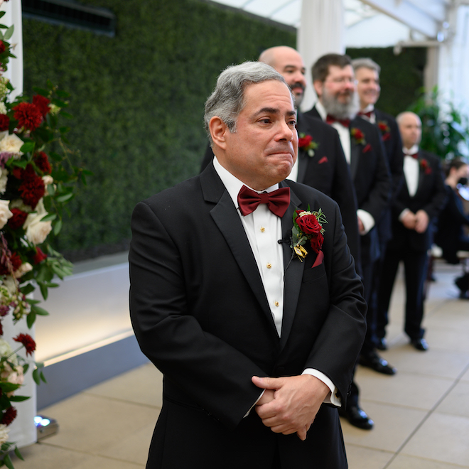 Groom watches bride walk down the aisle during a ceremony in the Sam Houston Hotel's Veranda Ballroom in Houston, TX.