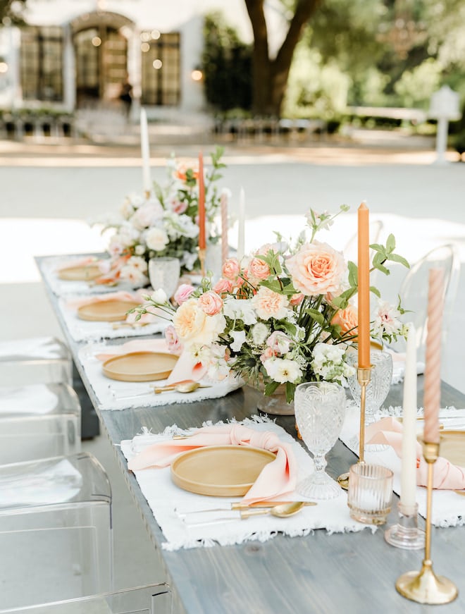 Pink, peach and white table settings and florals decorate the table outside the wedding venue. 