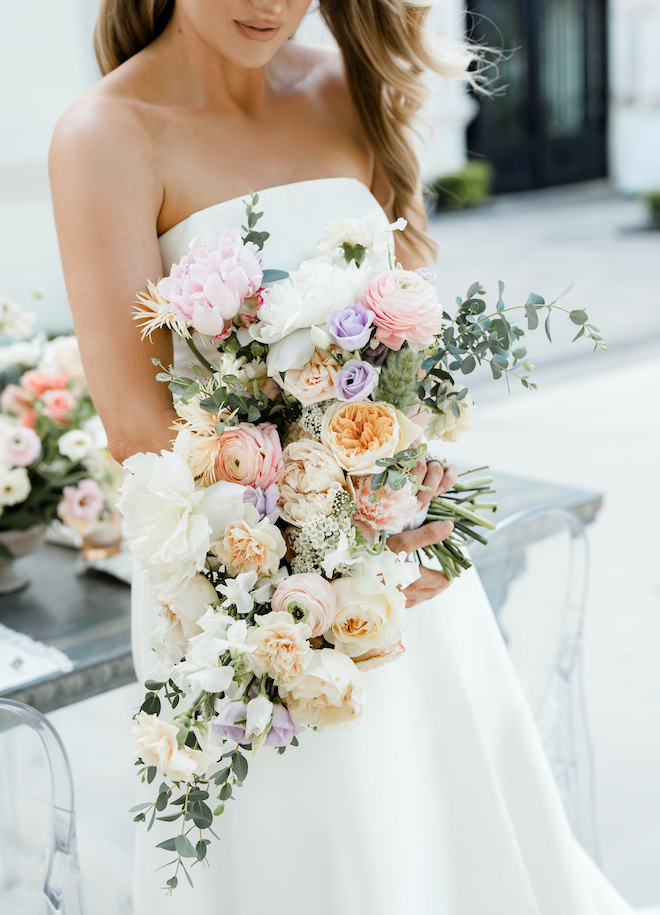 Peach, pink, lilac and white flowers fill the bride's wedding bouquet. 