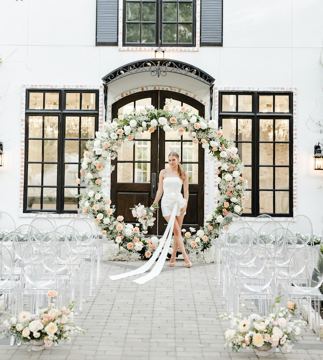 The bride holds her pastel wedding bouquet in front of a flower arch outside the wedding venue, The Peach Orchard. 